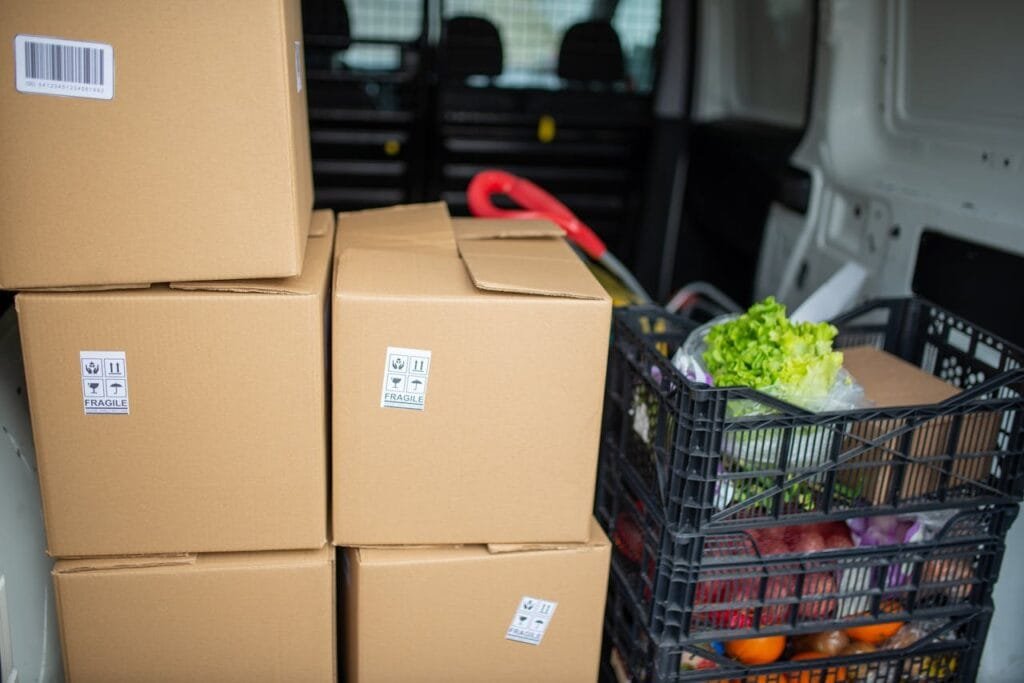 pexels-photo-7843989 Cardboard boxes and fresh produce being prepared for delivery in a van, highlighting logistics and farm-to-table movement.